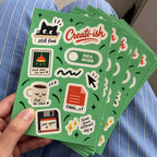 Stack of custom green sticker sheets featuring creative office, coffee, cat, cursor, and motivational designs.