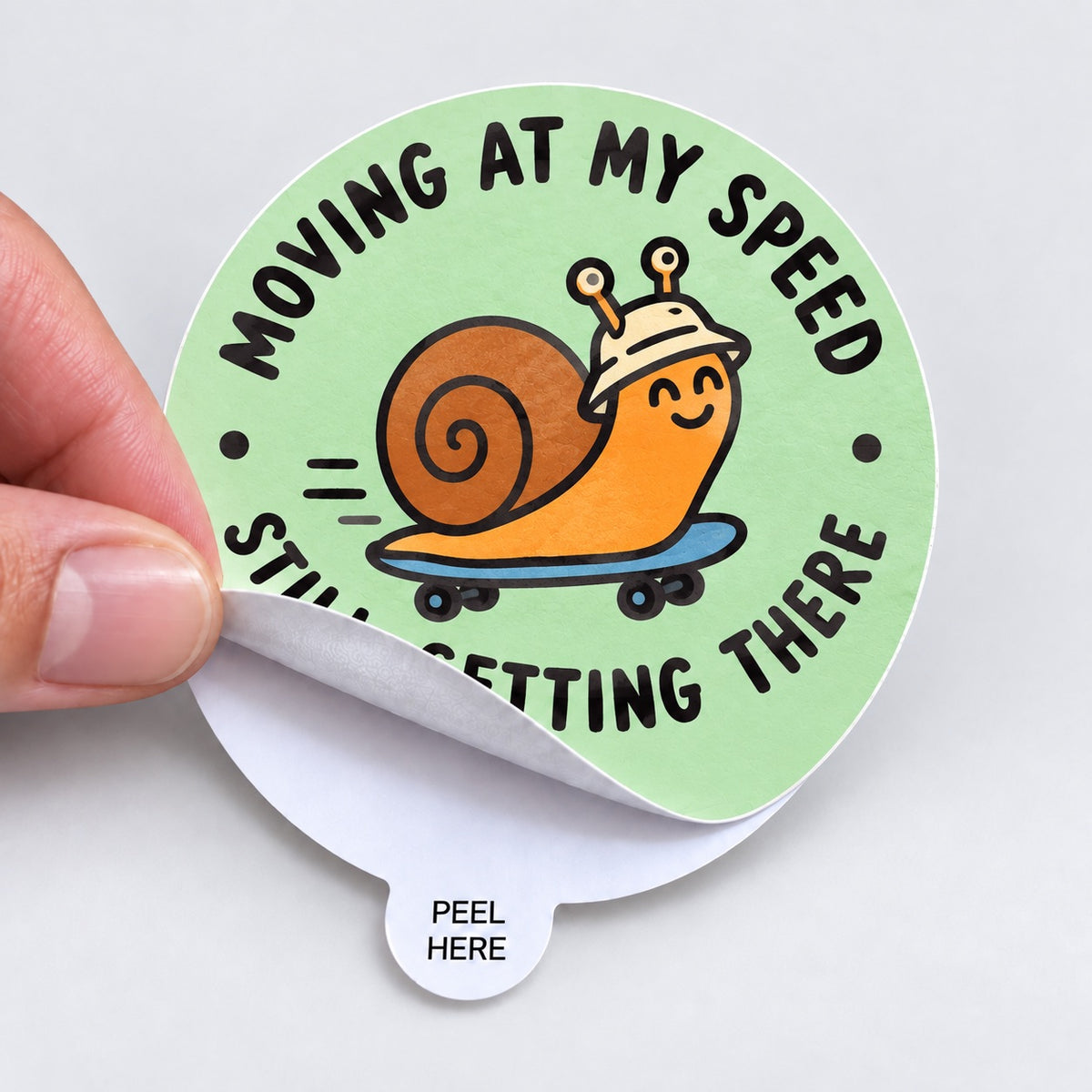 Custom round easy-peel sticker featuring a cheerful snail on a skateboard and a Peel Here tab.