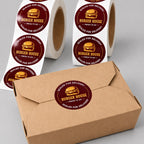 Custom round Burger House food delivery seal labels on rolls and applied to a kraft takeout box.