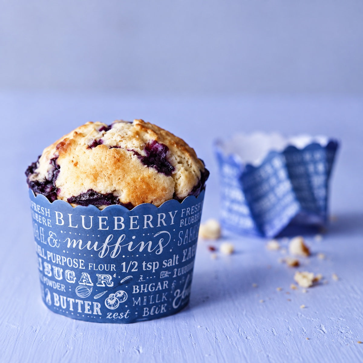 Custom printed paper bakery cup holding a blueberry muffin with colorful branded wrapper detail