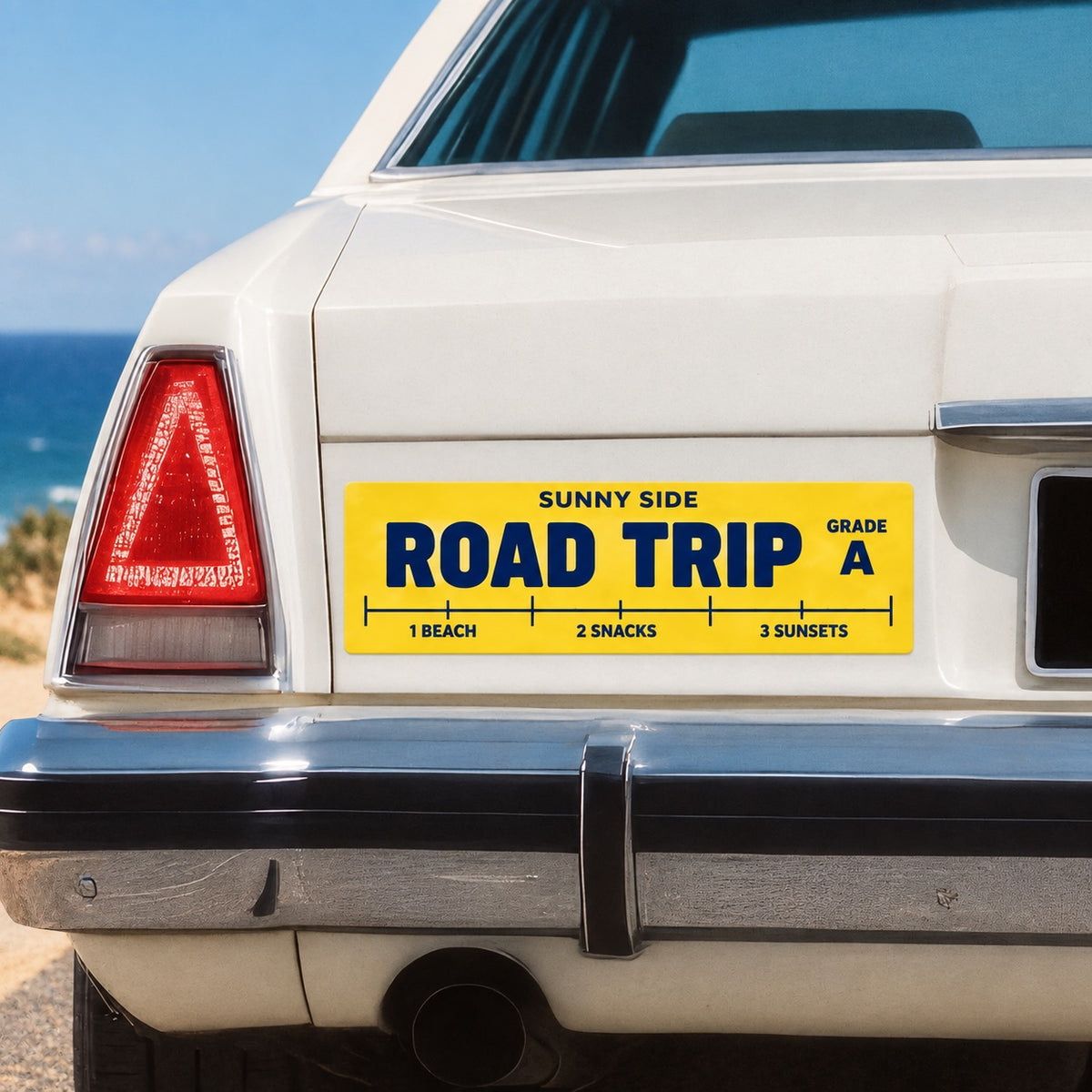 Yellow custom Road Trip bumper sticker applied to a white car near the coast.