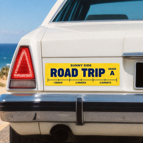 Yellow custom Road Trip bumper sticker applied to a white car near the coast.