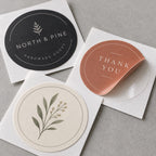 Custom round kiss cut logo and thank-you stickers in black, terracotta, and botanical designs on backing paper.