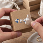 Blue and white custom logo transfer sticker applied to a small kraft paper jewelry box.