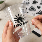 Black custom transfer logo sticker applied to a clear plastic cup while the transparent application film is peeled off.