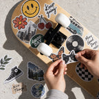 Assorted vintage-style custom vinyl die cut stickers decorating a skateboard while a cat sticker is applied.